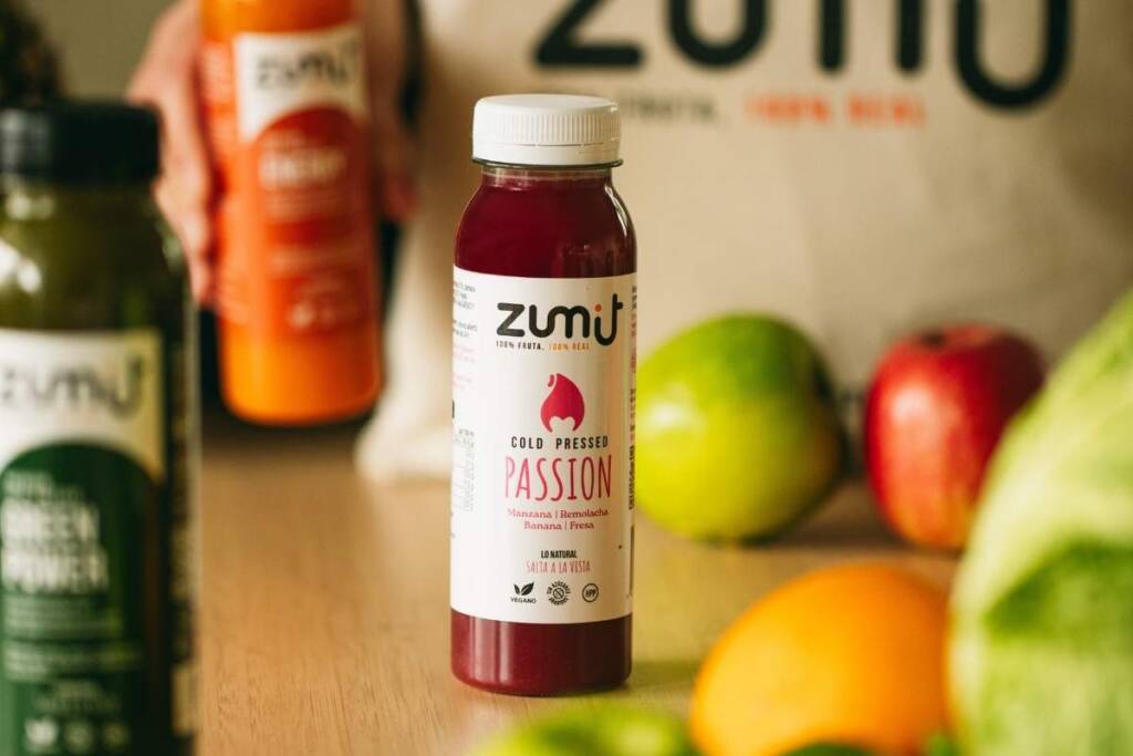 cold pressed Sumo de maracujá de Zumit numa mesa de madeira rodeada de fruta.