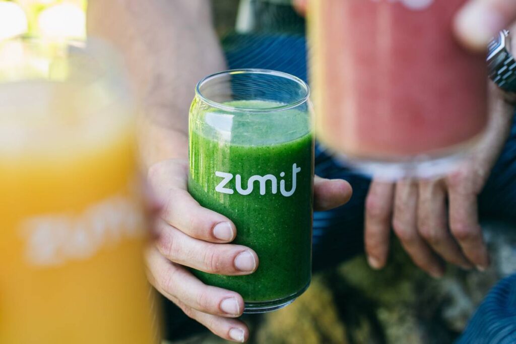 Smoothie Zumit Green Power com pepino, couve, ananás e espinafre segurado por uma mão